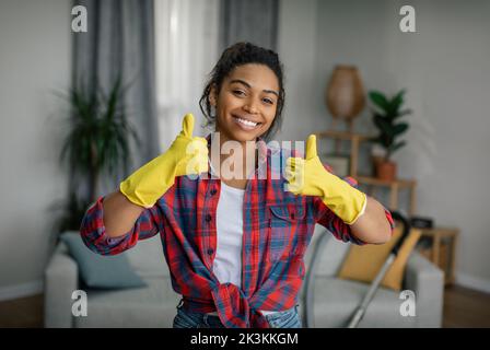 Excellent travail. Bonne jeune femme noire en gants montre le pouce vers le haut, aime le nettoyage résultat dans l'intérieur de salon Banque D'Images