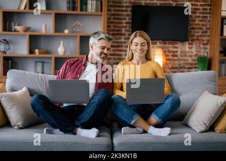 Un homme d'âge européen souriant regarde un ordinateur portable de dame, bavardant, profitez de votre temps libre, asseyez-vous sur un canapé dans le salon Banque D'Images