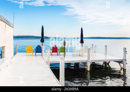 Quatre chaises en bois de couleur et parasol bleu sur une jetée en bois blanc, lac Léman près de Fontana, Wisconsin, Amérique. Banque D'Images