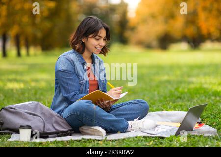 Portrait d'une femme arabe souriante étudiante se préparant à l'examen avec ordinateur à l'extérieur Banque D'Images