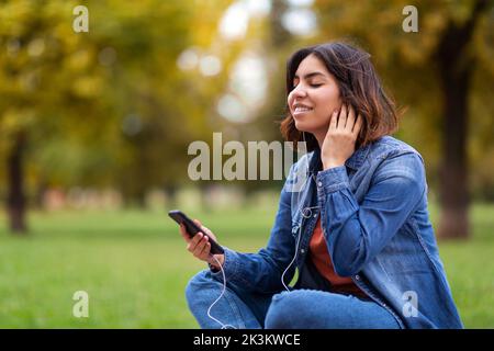 Portrait de la belle jeune femme du Moyen-Orient écoutant de la musique avec un smartphone à l'extérieur Banque D'Images