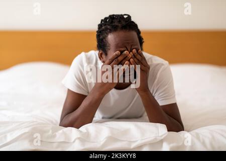 Un homme afro-américain fatigué se frottant les yeux tout en se réveillant au lit Banque D'Images