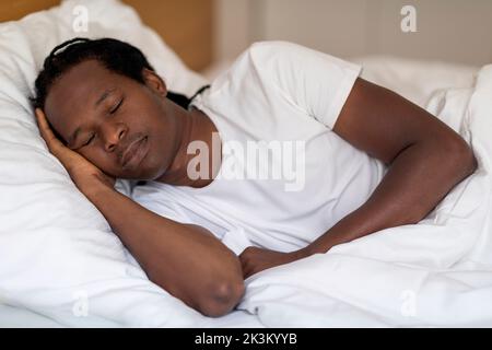 Portrait du jeune homme noir calme dormant dans un lit confortable à la maison Banque D'Images