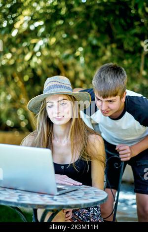 Portrait d'une jeune femme caucasienne avec son frère plus jeune posant à l'extérieur dans un jardin avec un ordinateur portable regardant l'information sur Internet. Style de vie conce Banque D'Images