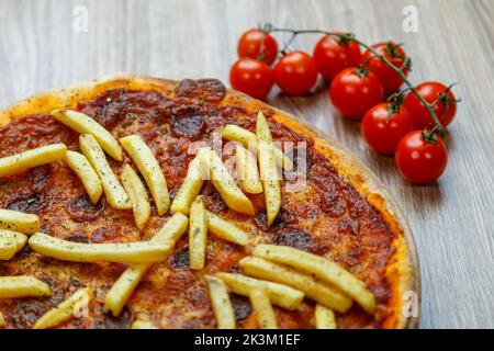 Une délicieuse pizza Patatosa avec des saucisses chaudes et des frites dans une sauce tomate avec des ingrédients à côté Banque D'Images