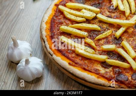 Une vue de dessus de Pizza Patatosa avec des saucisses chaudes et des frites dans la sauce tomate avec de l'ail à côté Banque D'Images