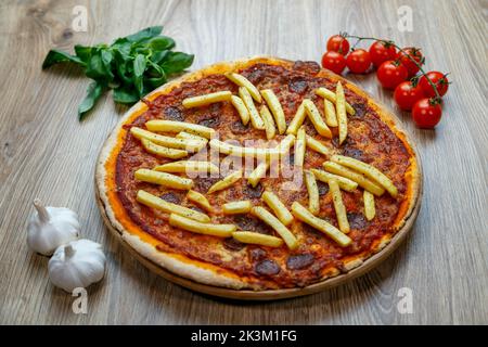 Une délicieuse pizza Patatosa avec des saucisses chaudes et des frites dans une sauce tomate avec des ingrédients à côté Banque D'Images