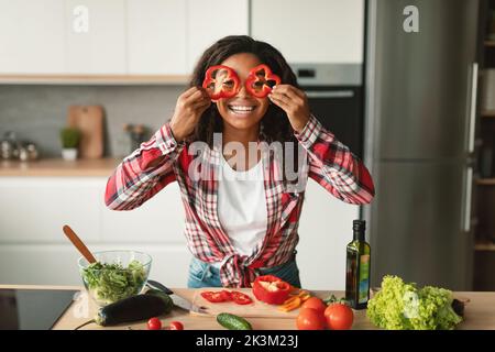 Une jeune femme afro-américaine heureuse met des morceaux de poivre à ses yeux comme des verres et s'amuser dans la cuisine Banque D'Images