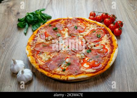 Une pizza au prosciutto Crudo, aux champignons, à la mozzarella, aux poivrons rouges, au persil avec des ingrédients à côté sur une table en bois Banque D'Images