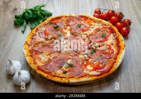 Une pizza au prosciutto Crudo, aux champignons, à la mozzarella, aux poivrons rouges, au persil avec des ingrédients à côté sur une table en bois Banque D'Images