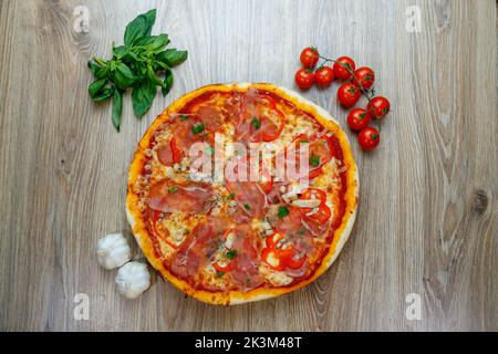 Une vue de dessus de pizza avec prosciutto Crudo, champignons, mozzarella, poivrons rouges, persil avec des ingrédients à côté sur une table en bois Banque D'Images