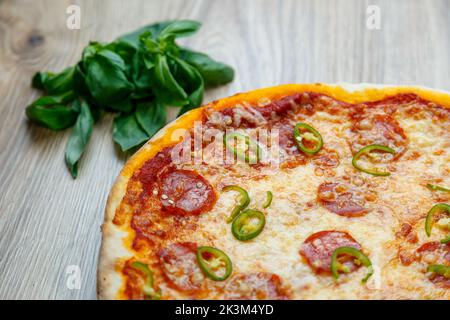 Une pizza Diavola avec salami, mozzarella, poivre vert chaud avec basilic à côté sur une table en bois Banque D'Images