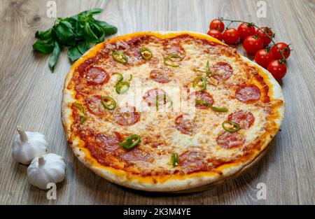 Une pizza Diavola avec salami, mozzarella, poivre vert chaud avec des ingrédients à côté sur une table en bois Banque D'Images