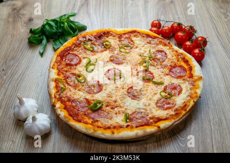 Une pizza Diavola avec salami, mozzarella, poivre vert chaud avec des ingrédients à côté sur une table en bois Banque D'Images