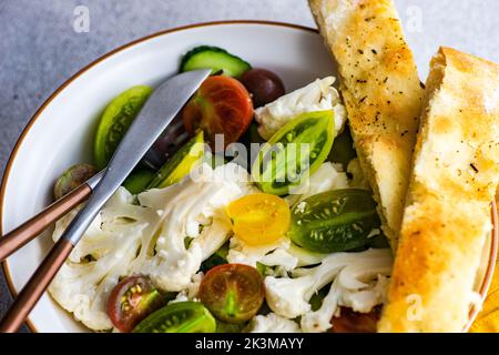 Salade de légumes saine dans le bol et pain de focaccia frais servi sur une table en béton Banque D'Images