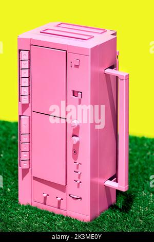Lecteur de cassettes vintage rose vif placé sur l'herbe verte contre fond jaune dans le studio Banque D'Images