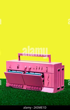 Lecteur de cassettes vintage rose vif placé sur l'herbe verte contre fond jaune dans le studio Banque D'Images
