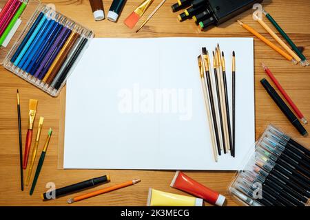Maquette d'artiste créatif sur table en bois . Pose à plat, vue de dessus avec carnet d'esquisses vierge avec espace de copie, crayons, pinceaux et peintures. Art Banque D'Images