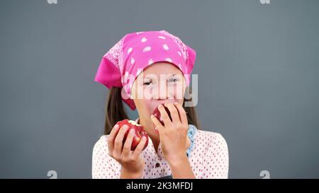 jolie fille paysanne tenant dans les mains deux grandes pommes rouges mûres, mange, les mord sur un fond gris dans le studio. Concept de nutrition saine. Photo de haute qualité Banque D'Images