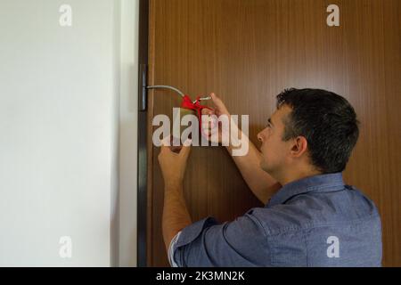 Photo d'un homme de main qui, avec un graisseur, lubrifie les charnières d'une porte qui grince. Les travaux ménagers et les activités à faire soi-même Banque D'Images