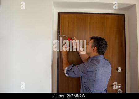 Photo d'un homme de main qui, avec un graisseur, lubrifie les charnières d'une porte qui grince. Les travaux ménagers et les activités à faire soi-même Banque D'Images