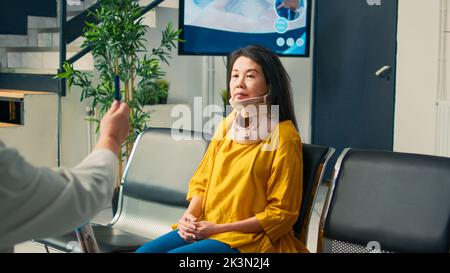 Médecin senior effectuant un examen de commotion cérébrale pour un patient avec col cervical, en utilisant un instrument avec lumière. Vérification des lésions de la vue et du cerveau avec une femme portant un corset de mousse médicale, visite de contrôle. Banque D'Images