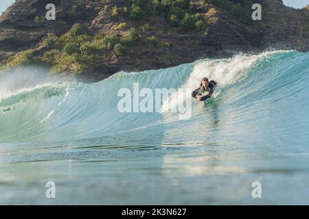 Un jeune homme en combinaison noire attrape une vague sur un bodyboard de planche de boogie à Piha Beach, Auckland, Nouvelle-Zélande. Banque D'Images