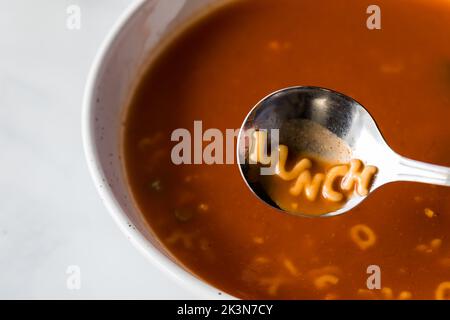 Un bol de soupe aux tomates à l'alphabet avec le mot déjeuner écrit dans la cuillère. Banque D'Images