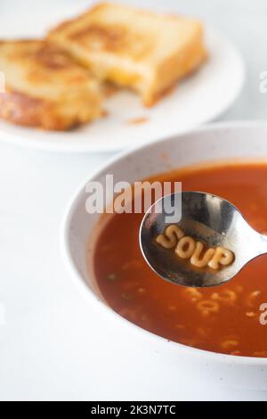Un bol de soupe aux tomates à l'alphabet avec le mot soupe écrit dans la cuillère. Banque D'Images