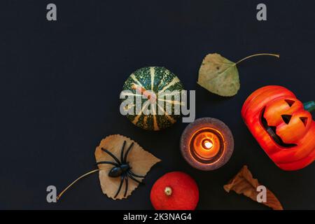 Halloween – plat festif avec Jack-O-Lantern, citrouilles, bougie, feuilles sèches et araignée sur table noire. Concept des vacances d'automne. Vue de dessus, espace de copie. Banque D'Images