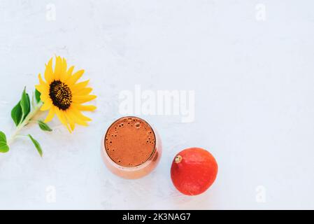 Smoothie de citrouille dans un verre, petit potiron et tournesol sur fond blanc texturé. Vue de dessus, plat, espace de copie. Banque D'Images