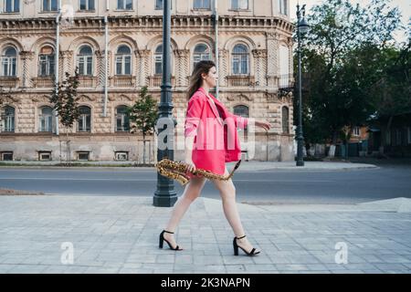 une jeune fille avec un saxophone marche le long de la rue de la ville Banque D'Images