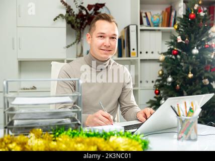 Un homme gai qui fait de la paperasse dans un bureau décoré à Noël Banque D'Images