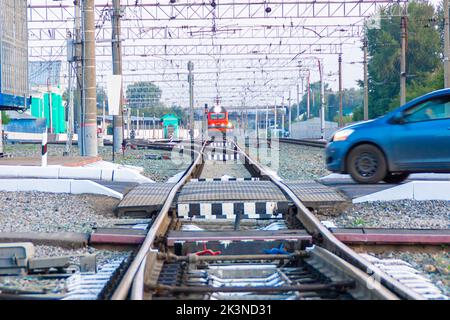 Kemerovo, Russie - 01 septembre 2022. Une locomotive rouge s'approche d'un passage de chemin de fer qui est sur le point d'être traversé par une voiture de tourisme, sélective f Banque D'Images