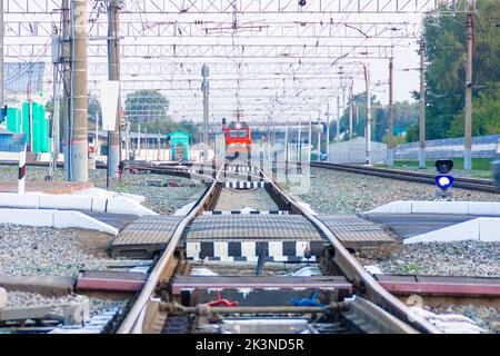 Kemerovo, Russie - 01 septembre 2022. La locomotive rouge des chemins de fer russes approche du passage à niveau en s'éloignant d'une petite gare, Banque D'Images