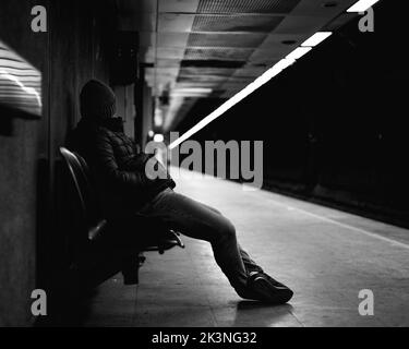 Vue latérale en niveaux de gris d'un homme assis sur un banc dans la plate-forme en attente de train Banque D'Images