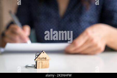 Maison en forme de mot Home porte-clés avec femme signant la vente et l'accord d'achat à l'arrière-plan. Banque D'Images