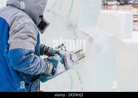 Faire des décorations de Noël. Le maître-sculpteur sculpte la sculpture sur glace avec scie à chaîne à partir d'un croquis fini. Banque D'Images