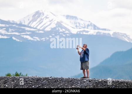 Touriste solitaire prenant des photos des montagnes Rocheuses canadiennes avec un téléphone mobile; Muncho Lake; Colombie-Britannique; Canada Banque D'Images