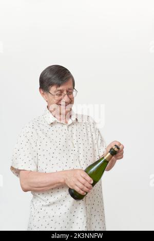 Homme hispanique senior souriant en tenant une bouteille de champagne ou de cidre et une paire de verres. Concept de toast festif. Banque D'Images