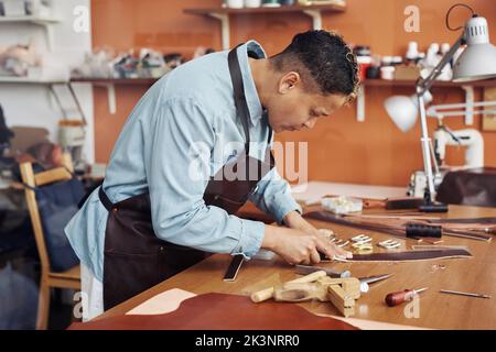 Vue latérale d'un artisan moderne créant une ceinture en cuir à la main dans un atelier, espace copie Banque D'Images