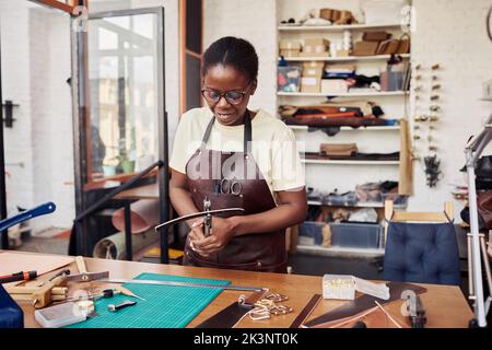 Portrait à la taille de la femme artisanale noire poinçonné dans une ceinture faite à la main dans un magasin de maroquinerie, espace de copie Banque D'Images