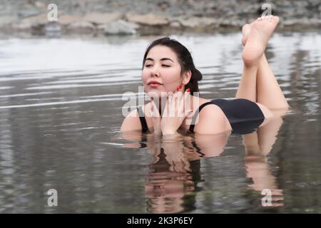 Modèle jeune adulte complet en maillot de bain noir une pièce couché et détente dans l'eau minérale dans la piscine extérieure du centre thermal Banque D'Images