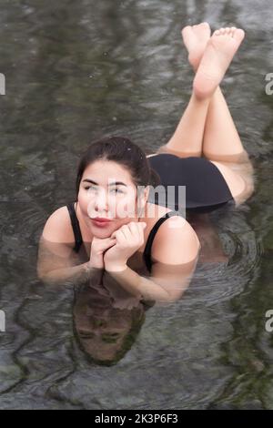 Femme en surpoids dans un maillot de bain noir d'une pièce couché, détente dans l'eau minérale géothermique dans la piscine extérieure balnéothérapie spa Banque D'Images