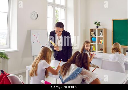 Une enseignante amicale fait le tour de la salle de classe pendant la leçon et donne des conseils aux élèves. Banque D'Images