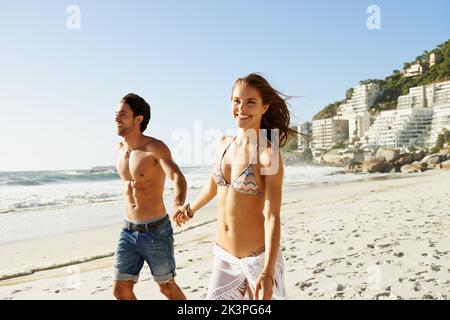 Trouver l'endroit idéal pour un séjour romantique sur la plage. Un jeune couple qui marche le long de la plage tient les mains. Banque D'Images