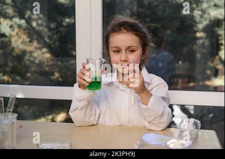 Mignon petite fille, chimiste conduit une réaction chimique avec le soda et l'acide citrique, étudie la chimie dans le laboratoire scolaire Banque D'Images