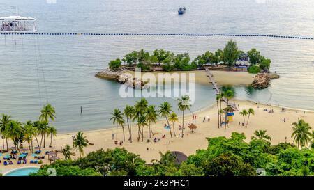 Vue aérienne de la plage de Siloso à Sentosa, Singapour. Les gens s'amusent sur le sable fin et les eaux calmes. Un pont suspendu relie à une petite île Banque D'Images