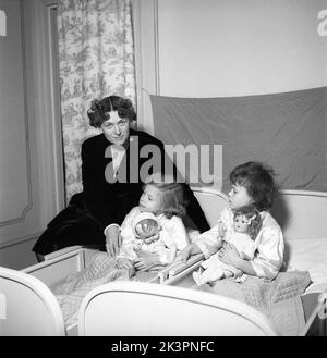 Mère dans le 1940s. Une scène de la chambre des enfants où les deux filles sont nichées dans le lit. Ils ont chacun une poupée. Les lits sont les lits extensibles classiques où la longueur peut être ajustée à mesure que les enfants grandissent et plus longtemps. Suède 1946 Kristoffersson réf. X123-1 Banque D'Images