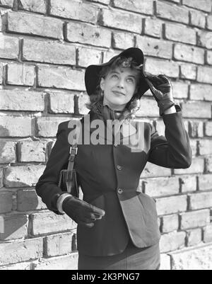 Tendance en 1950s. Une jeune femme vêtue d'une veste avec une taille mince visible, boutonnée avec trois butons. Elle porte un chapeau assorti et une écharpe autour de son cou, des gants en cuir noir et un sac à main. Suède 1952 Kristoffersson Réf. 38K-20 Banque D'Images